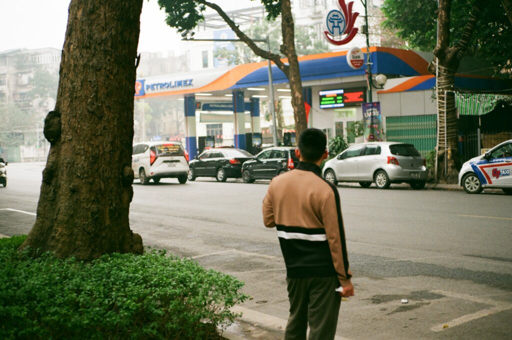 Man standing on street near gas station with cars.
