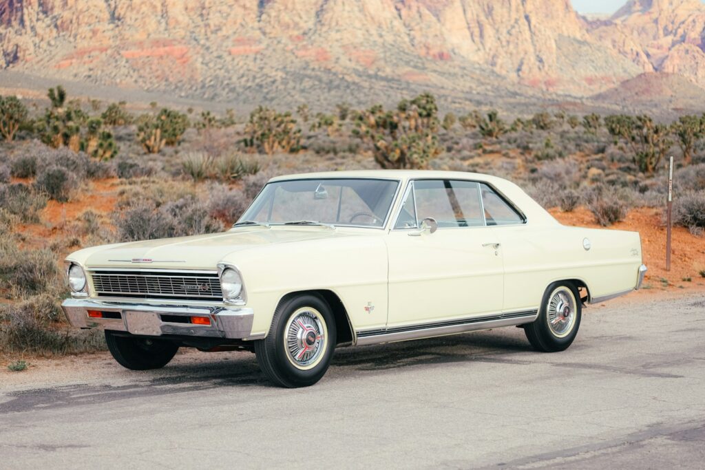 Vintage cream car parked on desert road with mountains.