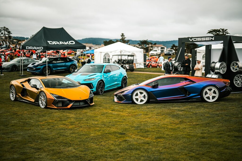 Three sports cars parked on grassy field with tents.