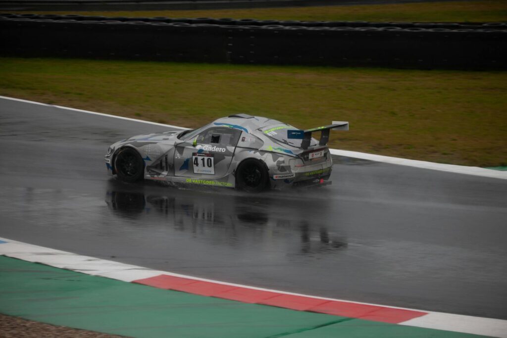 A race car speeds through a rainy track with blurred motion in an exciting motorsport event.