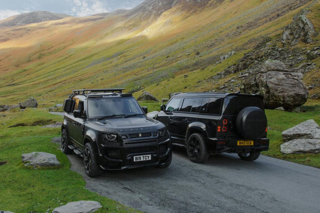 Two black Land Rover Defenders parked in a picturesque valley, showcasing rugged terrain.