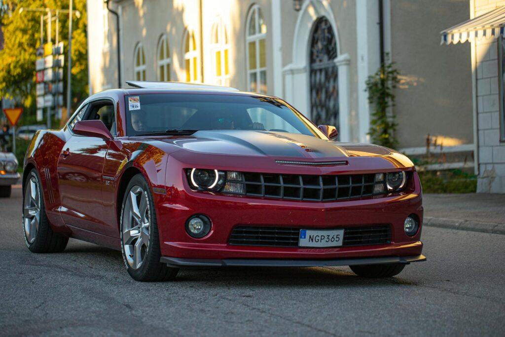 A striking red Chevrolet Camaro parked on a city street reflecting golden sunset light.