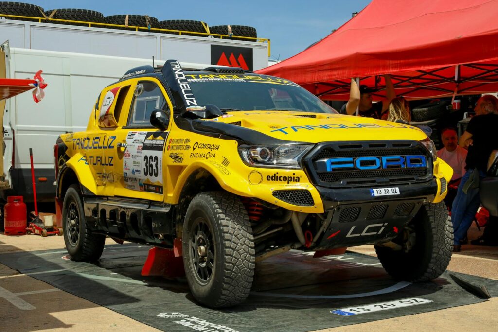 A vibrant yellow rally car on display at an outdoor racing event during the day.