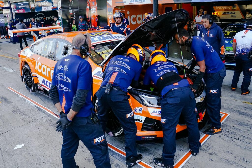 Race mechanics work vigorously on sports car in pit lane during competition.