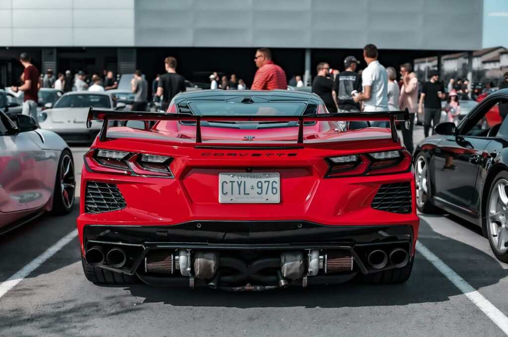 A striking red Corvette sports car parked in an urban car event surrounded by people.