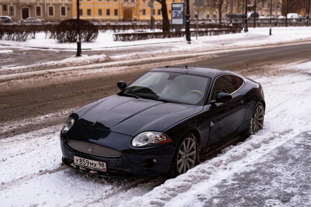 Black Jaguar parked on snowy city street, showcasing urban winter scene.