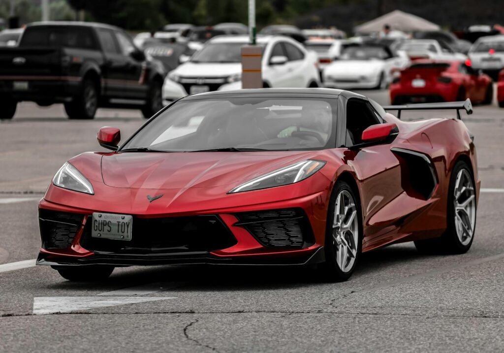 Dynamic shot of a red Chevrolet Corvette C8 in a busy urban parking lot during the day.