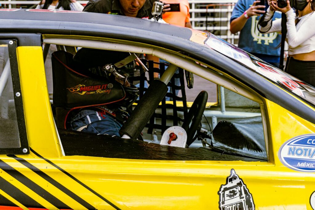 A professional driver wearing a helmet sits in a yellow race car during a motorsport event.