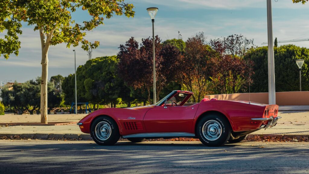 Side view of a classic red Chevrolet Corvette convertible parked outdoors under a sunny sky.