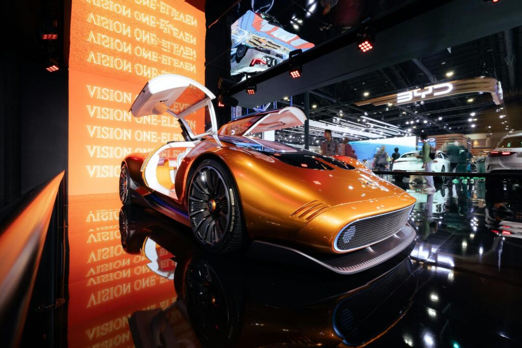 A sleek futuristic concept car in vivid orange displayed at an international motor show.