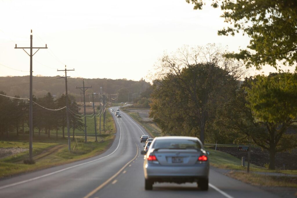 Cars driving on a peaceful rural road in Spring Grove, Illinois at sunset, surrounded by nature.