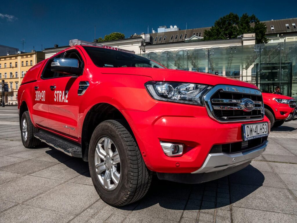 Red fire brigade vehicle parked in a city square under a bright blue sky.