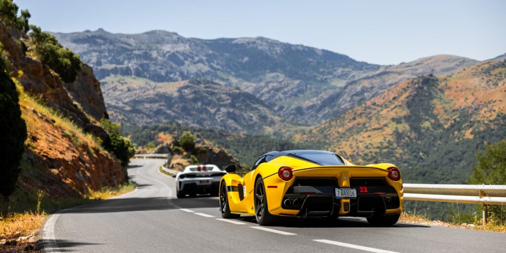 Luxury sports cars driving on a scenic mountain road during the day.