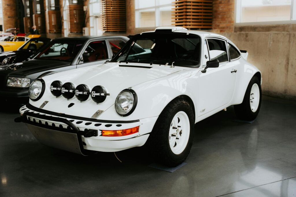 A vintage white rally car with extra headlights displayed indoors at an automotive exhibit.