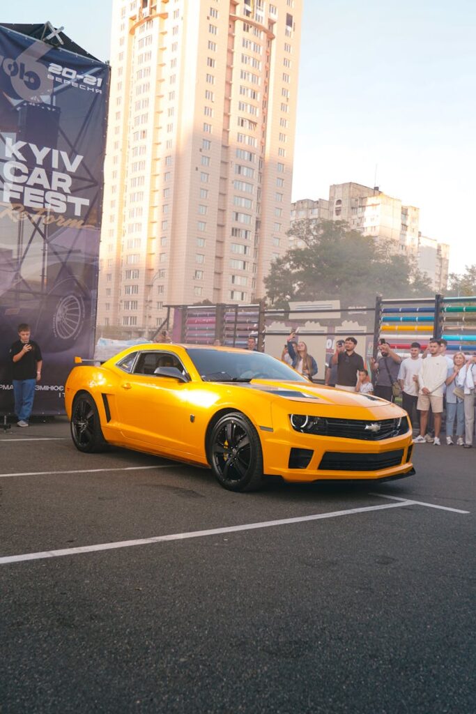 A vibrant yellow sports car displayed at the Kyiv Car Fest 2021 amid a crowd and urban backdrop.