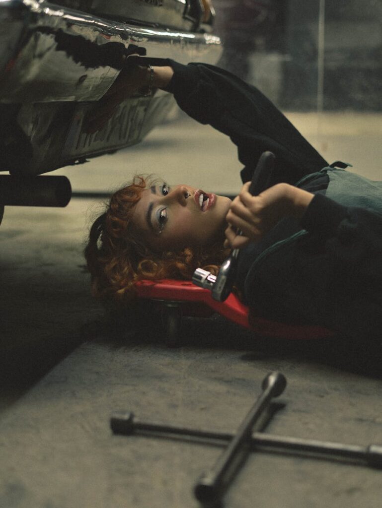 A young adult mechanic working underneath a car with automotive tools in a garage setting.