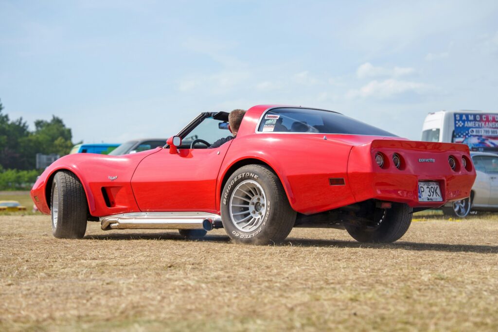 Rear view of a red vintage corvette on dry grass.