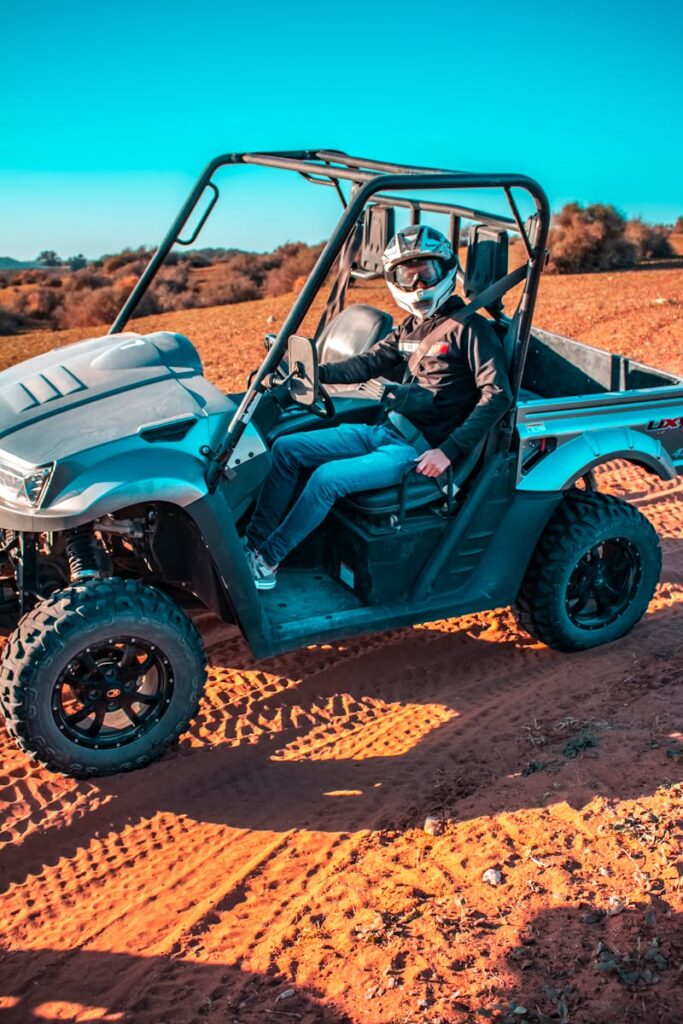A man wearing a helmet drives an ATV across the sunny Moroccan desert landscape, showcasing adventure and thrill.