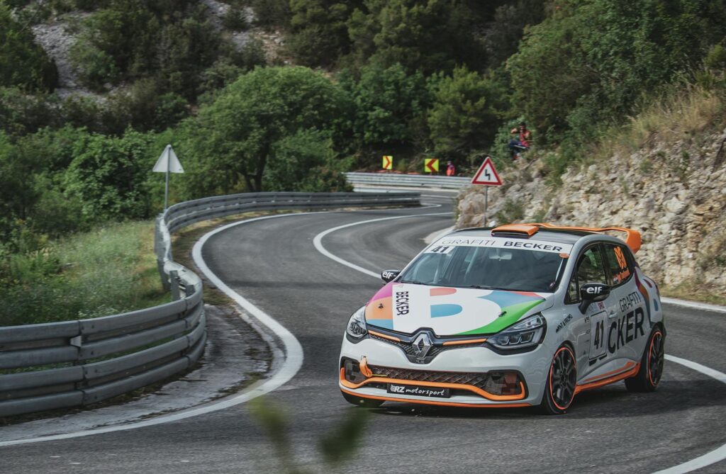 Renault rally car with colorful livery taking sharp mountain road turn during race.