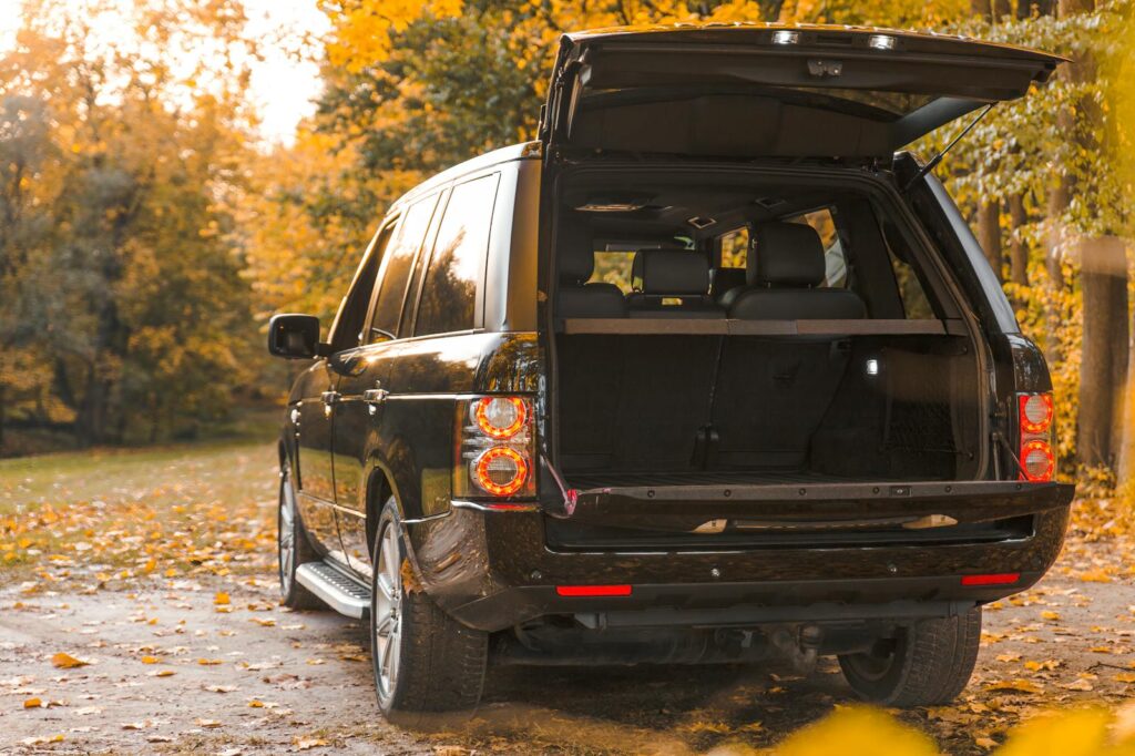 A black SUV with open trunk parked on a leaf-covered road in autumn forest setting.