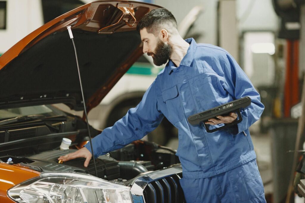 Professional mechanic examining a car engine under an open hood in a garage setting.