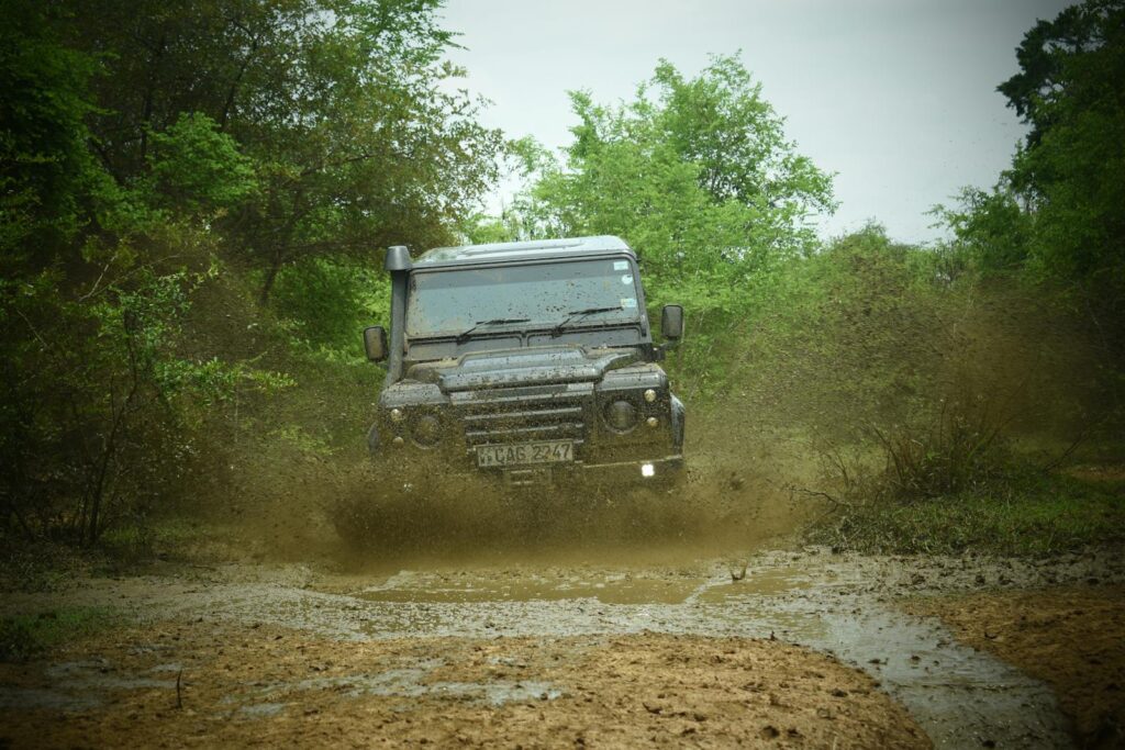 Land Rover SUV navigating a muddy dirt road through the lush forest.
