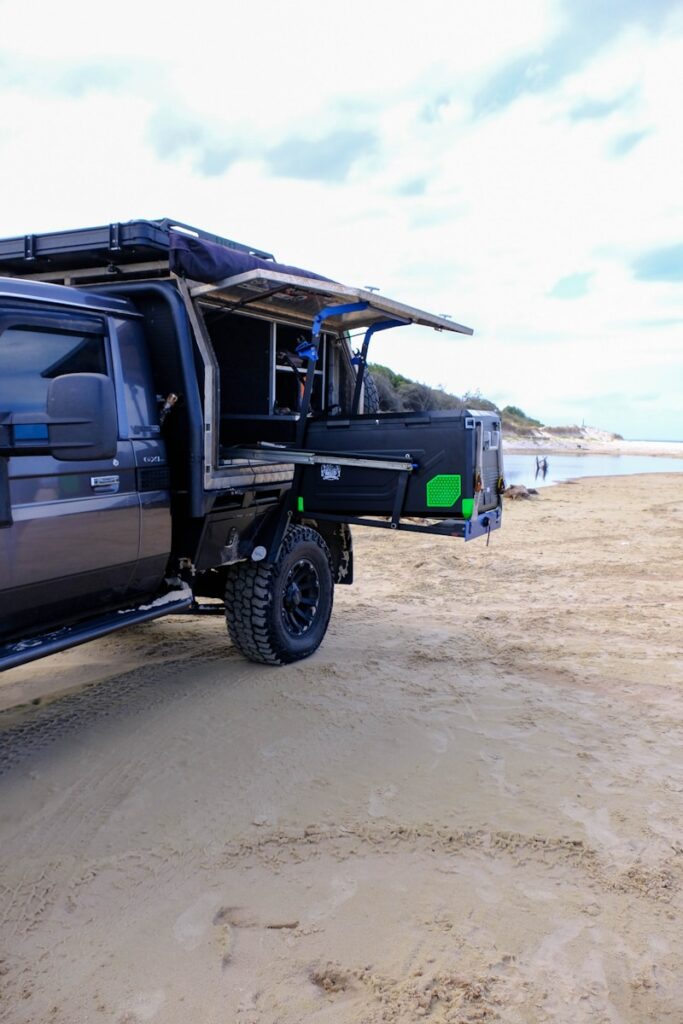 Dark grey truck with camper setup on beach.