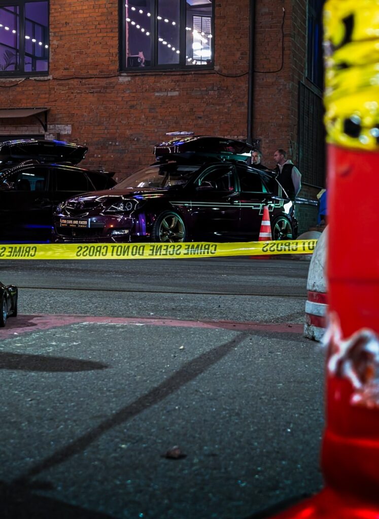 Crime scene tape surrounds damaged cars at night.