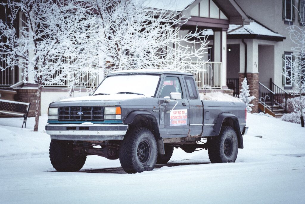 A classic Ford truck parked in a snowy, winter neighborhood, showcasing frosty outdoor conditions.