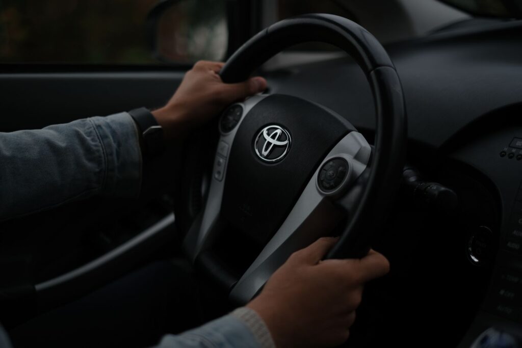 Hands on a Toyota steering wheel, closeup inside a vehicle. Darkened mood.