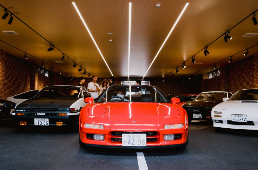 A selection of vintage Japanese cars displayed at an indoor car exhibition with people admiring them.