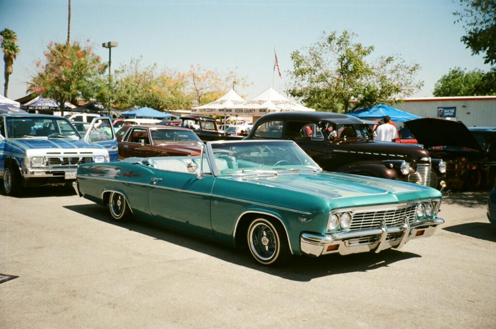 A vintage Chevrolet Impala showcased at an outdoor car show under sunny skies.