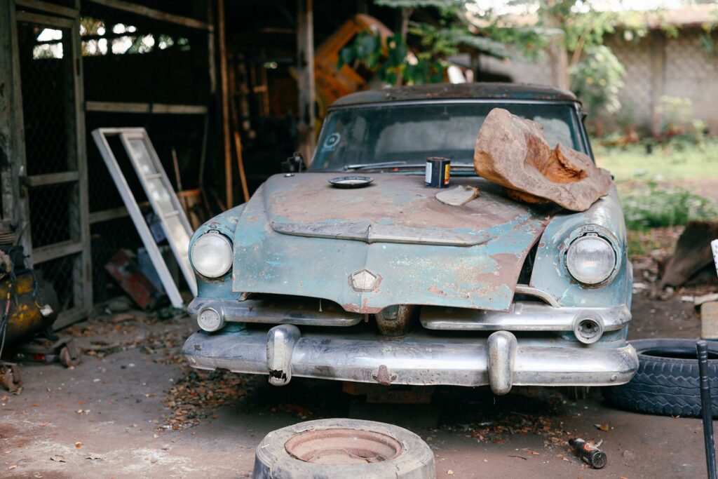 A rusty, abandoned vintage car in a workshop, surrounded by tires and tools, evoking nostalgia.