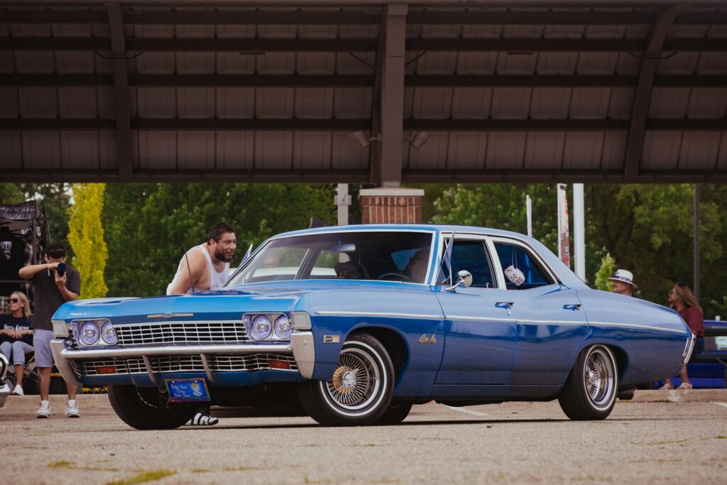 A vibrant blue vintage Chevrolet car displayed at an outdoor car show with people admiring.