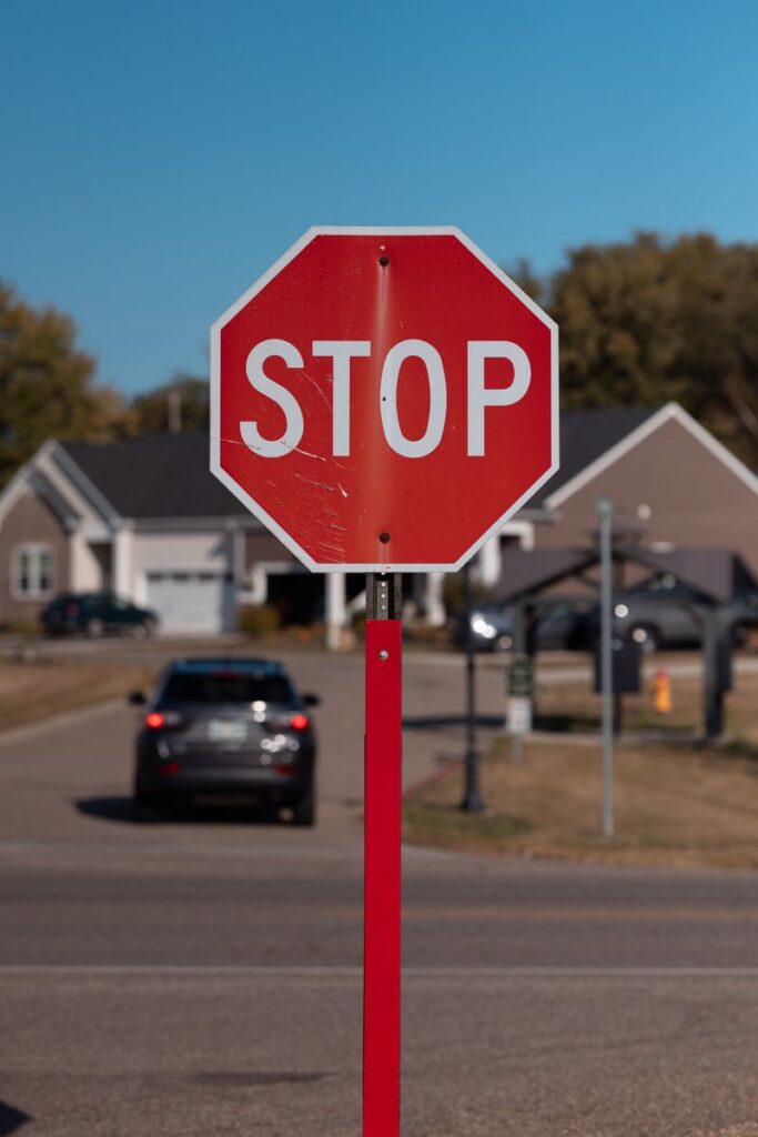 A bright red stop sign on a suburban street with cars and houses in the background.