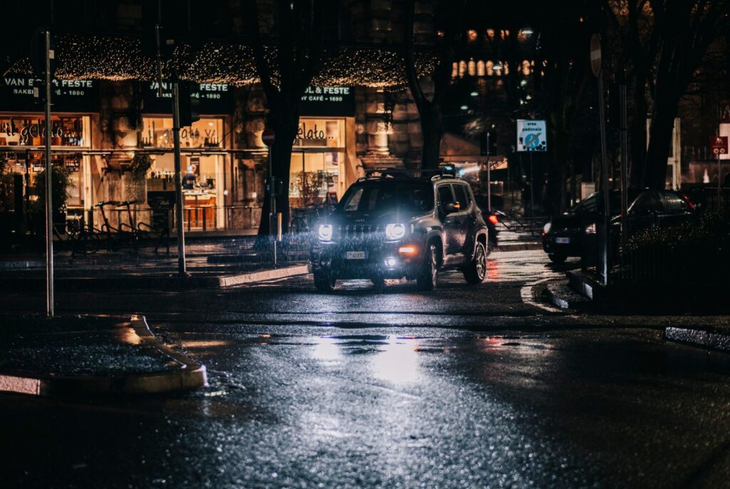 A rainy night city street scene with cars and bright storefronts, capturing reflections and moody lighting.