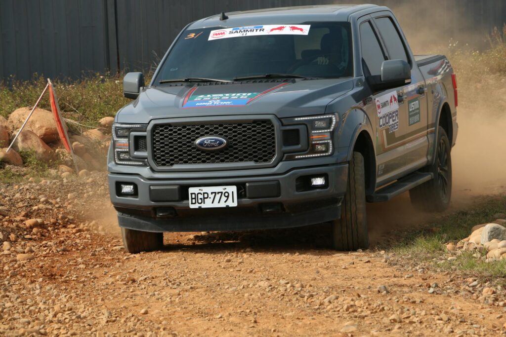 Gray Ford F150 driving fast on a rocky dirt road during an offroad adventure race.