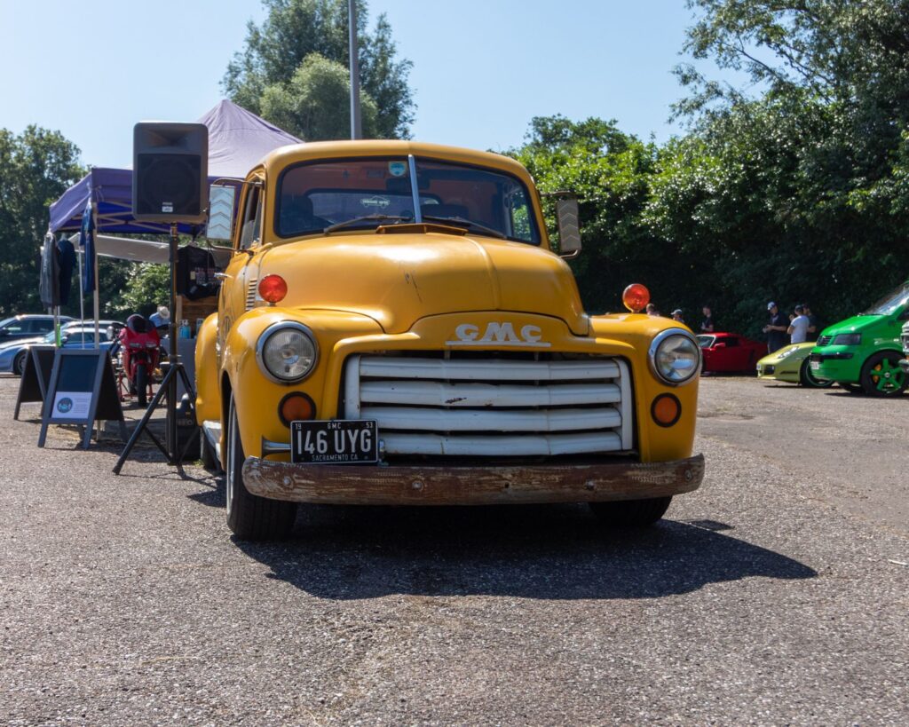 A classic yellow truck displayed at an outdoor car show under a sunny sky.