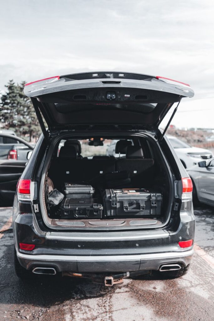 Open trunk of an SUV filled with equipment cases, parked outdoors under a cloudy sky.