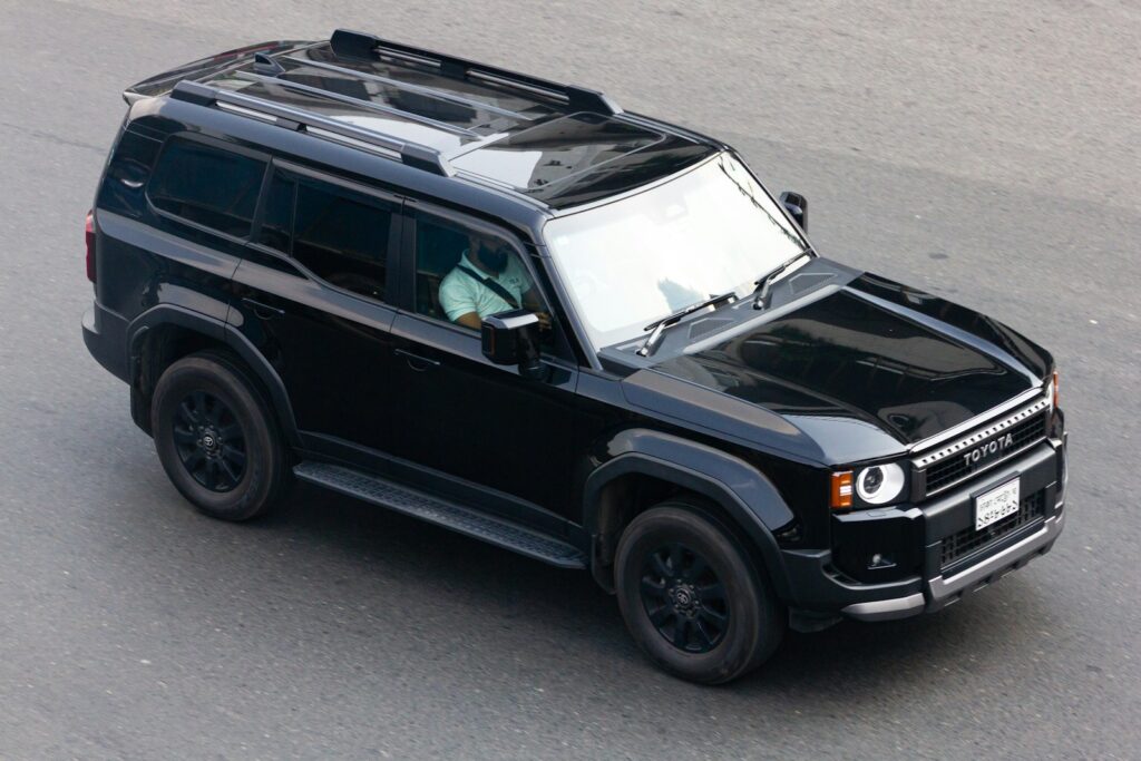 A black toyota suv with roof racks drives on pavement.