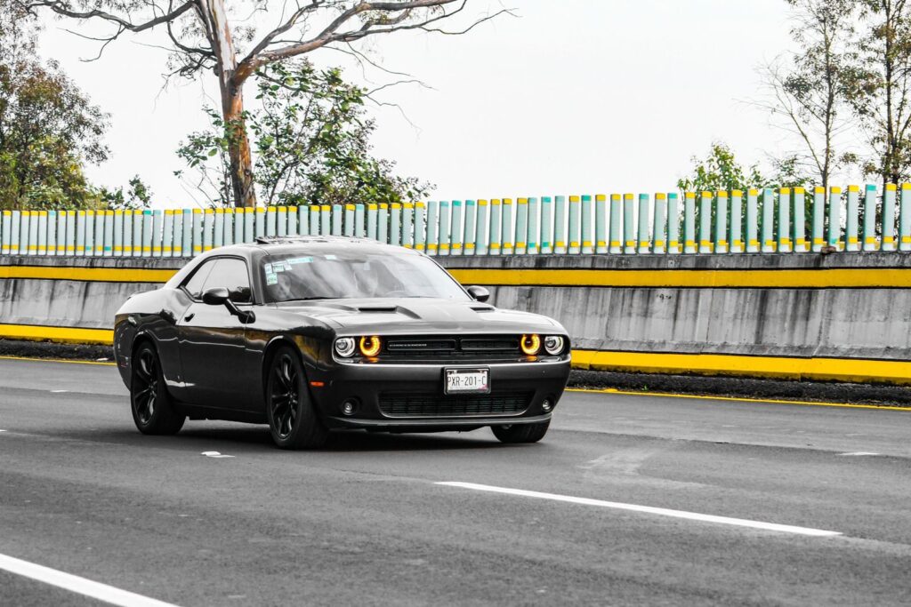 A modern black Dodge coupe driving on an open city road with vibrant surroundings.
