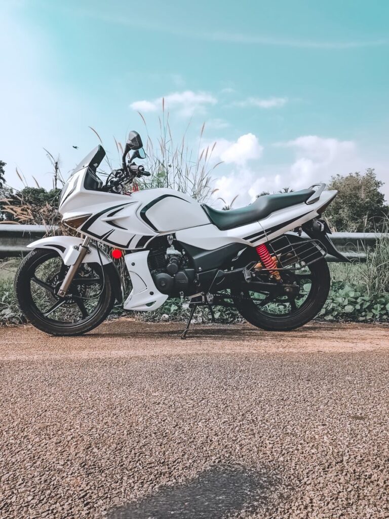 Side view of a white motorcycle on an empty rural road, under a clear blue sky.