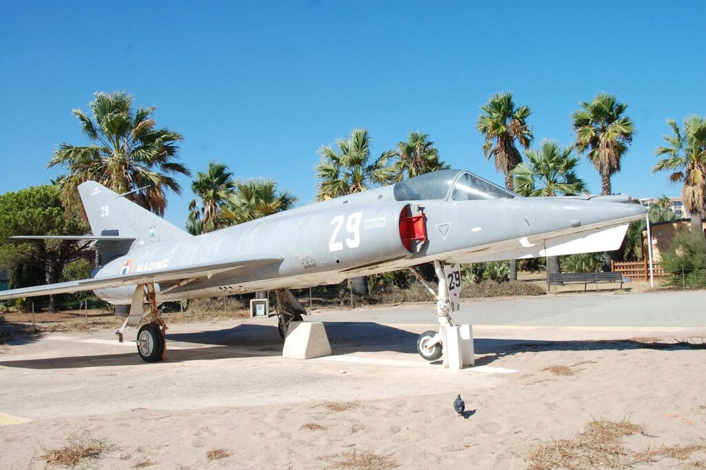 Historic military jet on display in sunny Saint-Tropez, France, surrounded by palm trees.