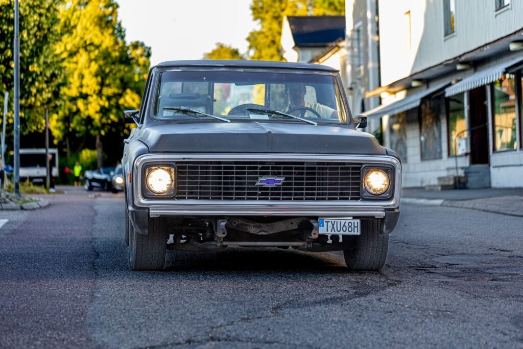 Classic Chevrolet truck driving on a sunlit urban street in daytime.