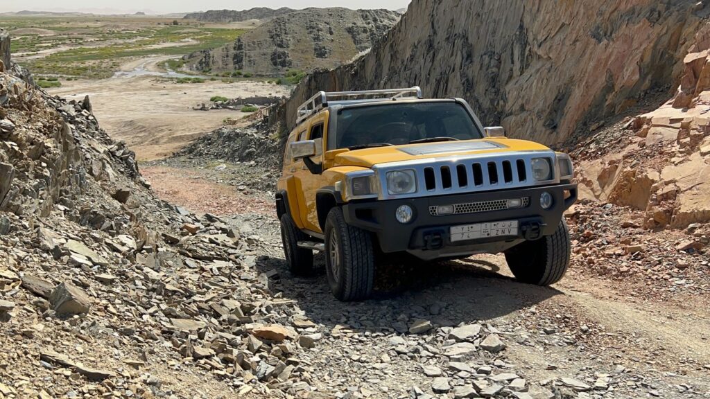 A yellow SUV navigating a rugged, rocky off-road terrain under a bright sky.
