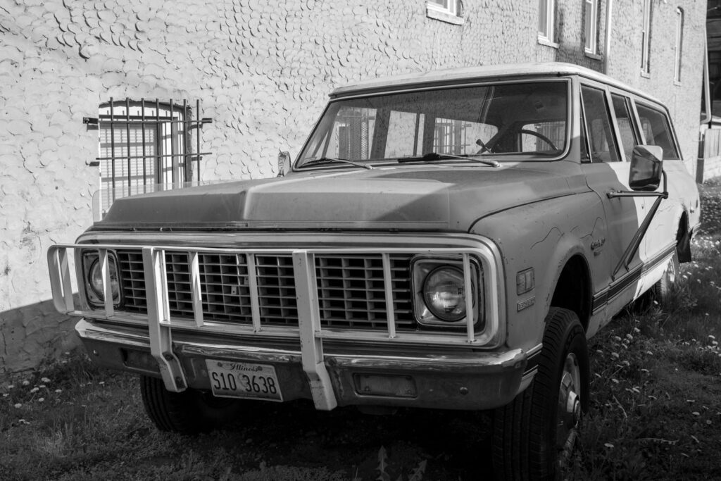 Black and white image of a vintage SUV parked against a textured urban wall.