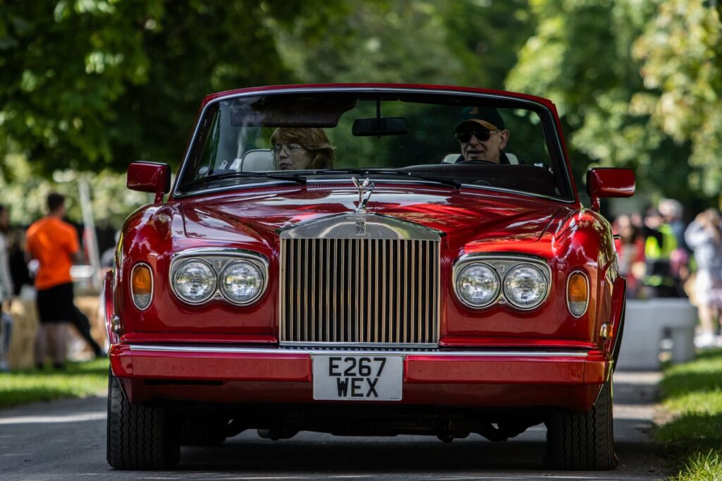 A classic red Rolls-Royce convertible driving down a city street with senior passengers.