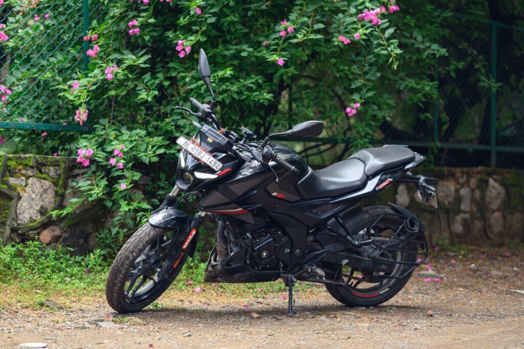 A sleek black motorcycle parked beside a lush garden fence adorned with vibrant pink flowers.