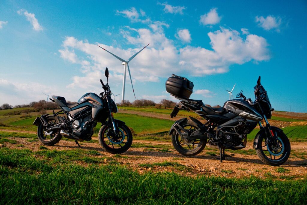 Two motorbikes parked in a scenic rural area with wind turbines under a clear blue sky.
