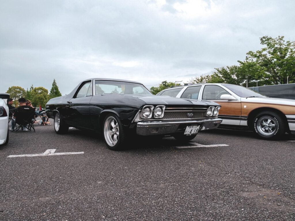Vintage black muscle car showcased at an outdoor car meetup under cloudy skies.